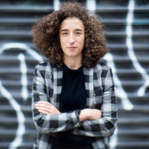 Lorena Russi headshot in plaid standing in front of a spray-painted grate